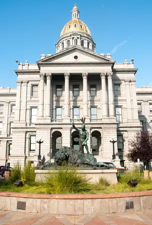 The east entrance of the capitol building showing a statue of a bison and a native american